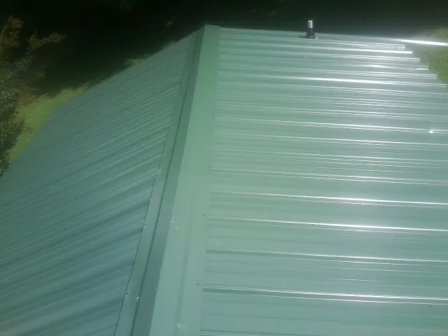 New green metal panels meeting at the ridge of a roof — Flat Roof Repair work by our crew in Rochelle