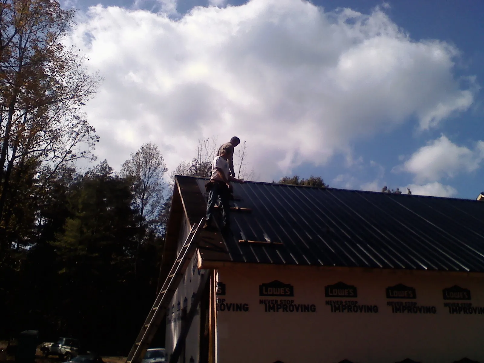 Roofer fastening dark metal panels high against a cloudy sky, from a Roof Inspection job in Rochelle